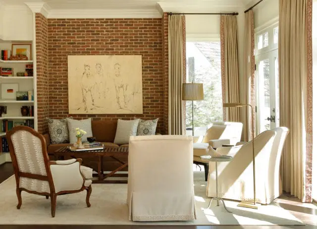 Living room with exposed brick wall, neutral-toned furniture including a sofa, armchairs, and a slipcovered chair, and a large painting of horses above the sofa.