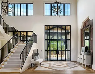 Grand foyer with a white staircase featuring black metal railings, a white upholstered bench, and a large black metal-framed glass door.