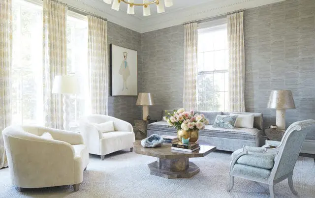 Living room with grey textured wallpaper, white upholstered armchairs, a light blue sofa, and a hexagonal coffee table with a floral arrangement.