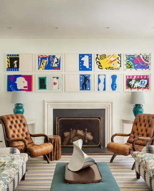 Living room with a fireplace, featuring a collection of framed Matisse Jazz prints above, two tufted leather armchairs, and patterned sofas.