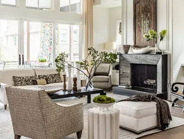 Living room with a large stone fireplace, white sofa, patterned accent chairs, and a dark wood coffee table with a vase of branches.