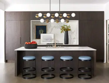 Dark wood paneled kitchen with white marble island, light blue bar stools, and a modern brass faucet.