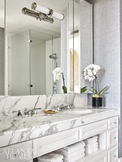 Double vanity with white marble countertop and backsplash, white cabinetry, and a glass-enclosed shower with white tile.