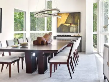 Modern dining room with dark wood table and chairs featuring white upholstery, large windows, abstract art, and a sculptural chandelier.
