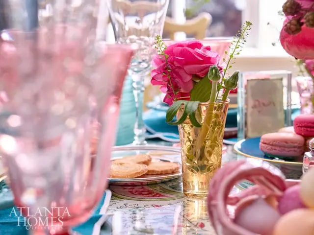 Table setting with pink glasses, gold vase with pink flowers, macarons, and cookies.