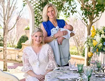 Two women and a baby posing for a portrait outdoors at a table set for a meal.