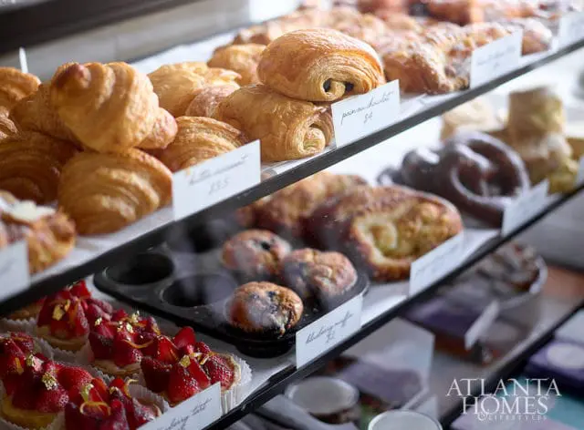 Display case filled with pastries including croissants, pain au chocolat, blueberry muffins, and strawberry tarts topped with gold leaf.