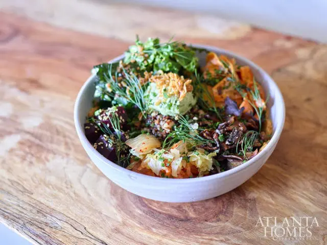 Close-up of a colorful grain bowl with beets, kimchi, sweet potatoes, mushrooms, and greens, garnished with dill and sesame seeds.