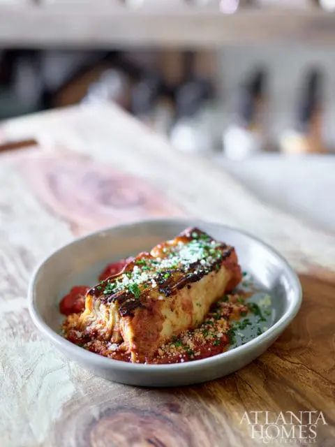 Lasagna with marinara sauce and grated cheese, served in a light gray bowl on a wooden surface.