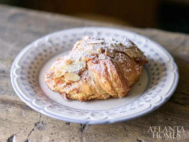 Almond croissant dusted with powdered sugar and sliced almonds on a blue and white patterned plate.
