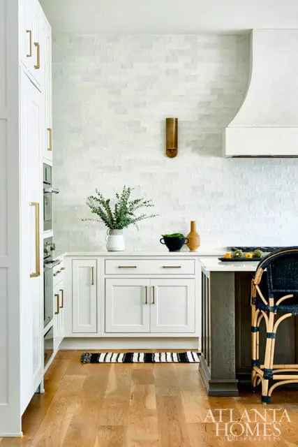 White kitchen with white subway tile backsplash, brass hardware, and a dark wood island with a rattan bar stool.
