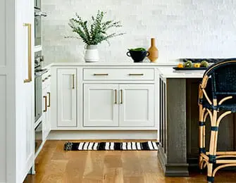 White kitchen with shaker cabinets, brass hardware, white subway tile backsplash, and a dark wood island with rattan stools.