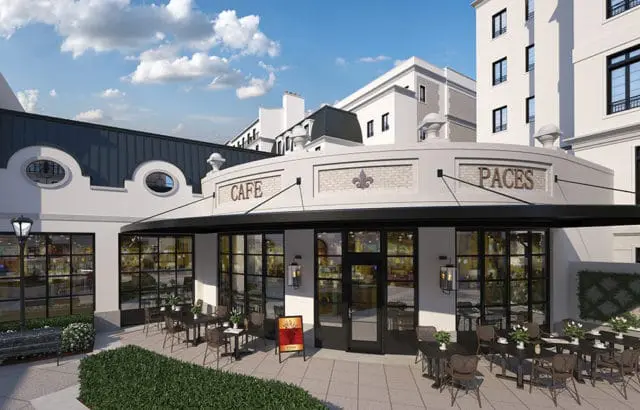 Cafe with a curved facade, black awning, and large windows. Tables and chairs are set up on the patio. The building is white with architectural details and the name "PACES" above the entrance.