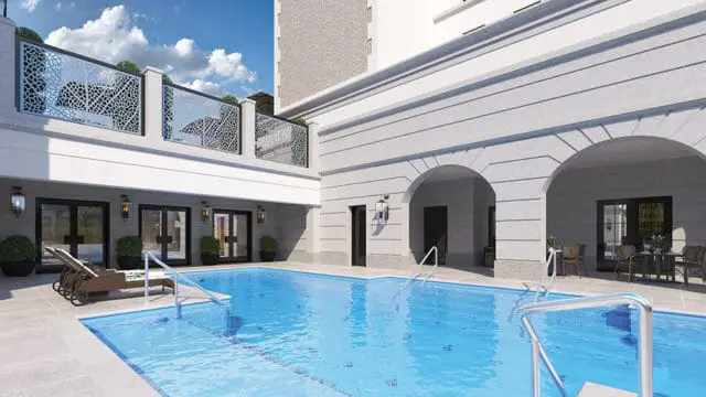 Courtyard swimming pool with lounge chairs and outdoor dining sets, surrounded by a building with arched entrances and decorative metal railings.