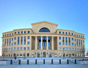 Beige stone courthouse with a curved facade, classical columns, and arched windows under a clear blue sky.