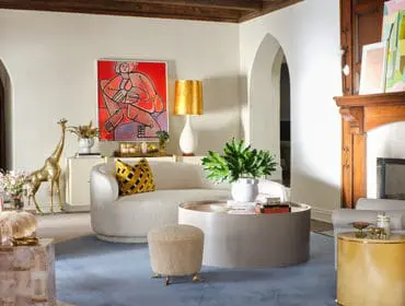 Living room with a plush pink armchair, a curved cream sofa, a round coffee table, and a brass giraffe statue. A large abstract painting hangs above a credenza.