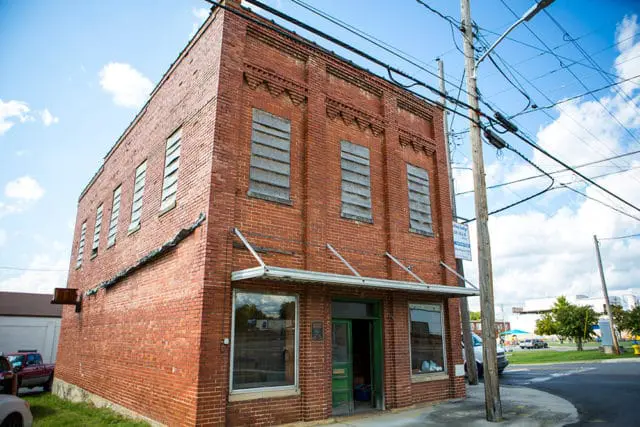 Two-story brick building with boarded-up windows and a green door, under a cloudy blue sky. A sign on a utility pole reads "Masonic Lodge 238"