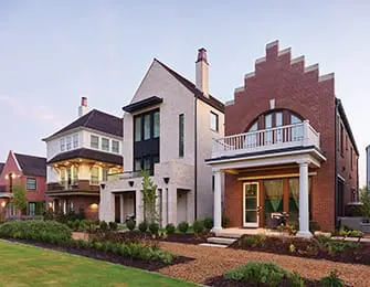 Row of diverse luxury homes with brick and stucco exteriors, pitched roofs, and varied architectural details, set against a twilight sky.