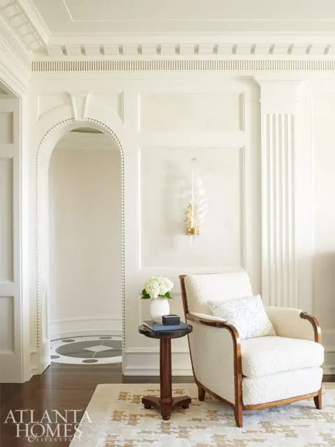 Cream boucle armchair with wood trim and decorative pillow next to a dark wood side table with a vase of white hydrangeas and books.