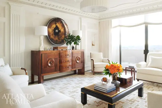 Living room with cream upholstered chairs, a dark wood buffet with decorative circular inlays, and a large circular artwork above the buffet.