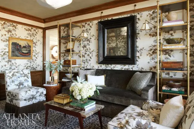Living room with floral wallpaper, dark velvet sofa, patterned armchairs, marble-topped coffee table, and gold shelving unit.