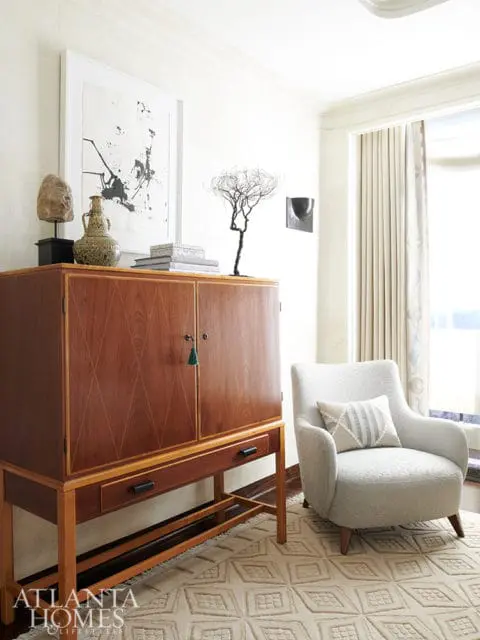 Living room with a mid-century modern wood cabinet, a light gray armchair with a patterned pillow, and a geometric rug.