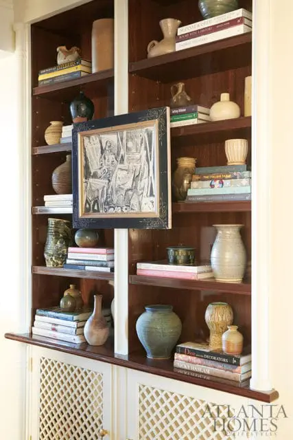 Built-in dark wood shelving unit displaying various ceramic vases, decorative objects, and books. A framed black and white sketch hangs centrally.