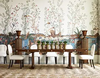 Dining room with a dark wood table set with potted plants and white chairs, against a wall with a scenic chinoiserie wallpaper.