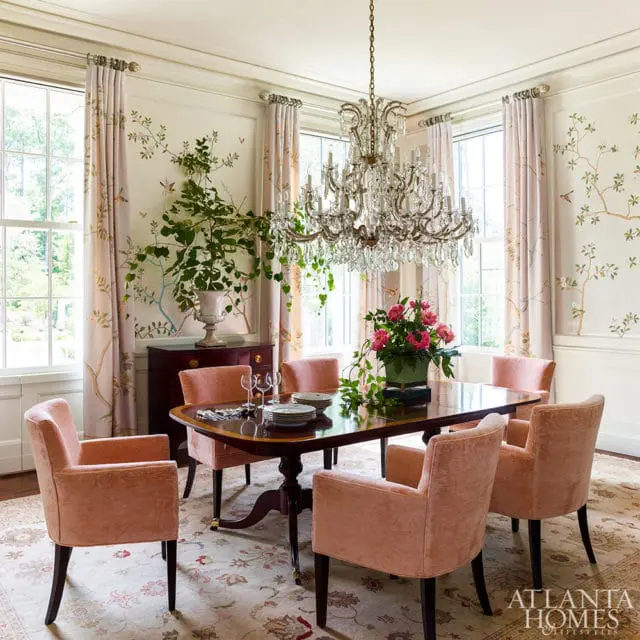 Dining room with a dark wood table, six upholstered chairs in a peachy-pink velvet, a crystal chandelier, and walls with a bird and branch mural.