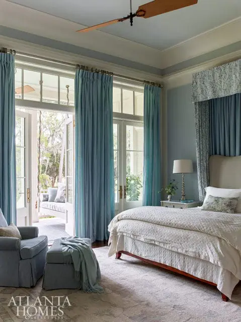 Bedroom with light blue walls, white bedding, and blue curtains. French doors open to a porch with a swing.