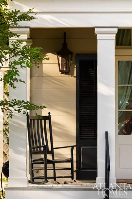 Front porch with a black rocking chair, hanging lantern, and white columns. A black shuttered door is visible behind the chair.