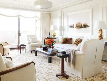 Living room with white slipcovered sofa, upholstered armchairs, dark wood coffee table, and large window with sheer curtains.