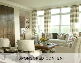 Living room with neutral-toned sofa and armchairs, a large window with striped curtains, and a wood-paneled accent wall.
