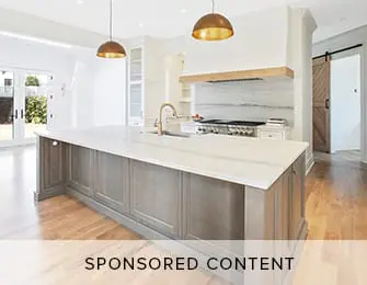Spacious kitchen with a large gray island topped with white marble, brass pendant lights, and a white range hood with wood accents.