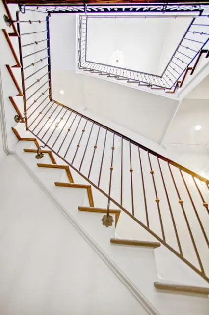 White staircase with dark metal railings featuring decorative floral accents and wooden treads, looking up towards a chandelier.