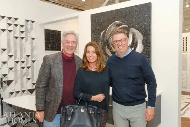 Three people pose in front of a mosaic art piece and patterned tile wall. A logo for Atlanta Homes & Lifestyles is visible in the lower left corner.
