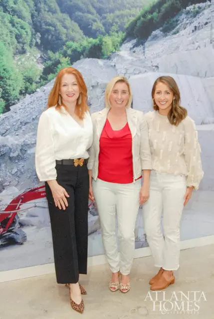 Three women stand in front of a mural depicting a quarry and forest.