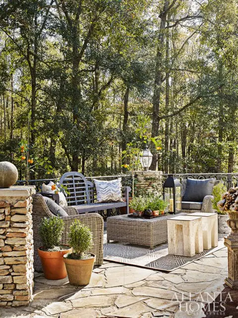 Stone patio with wicker furniture, bench, and coffee table surrounded by trees.