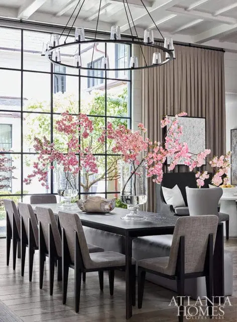 Dining room with dark wood table, upholstered chairs, large window with pink blossoms, and a circular chandelier.