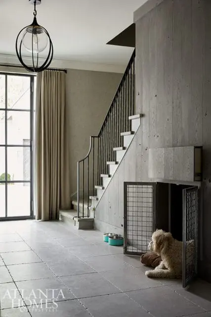 Modern entryway with concrete floors, a dog crate with a fluffy dog inside, and a staircase with black metal railings and wood paneling.
