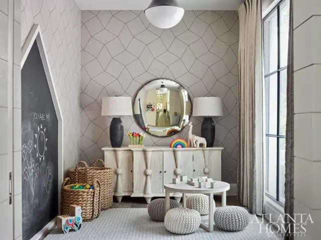 Playroom with geometric patterned wallpaper, a chalkboard wall, a distressed wood cabinet with lamps and toys, and a round coffee table with poufs.