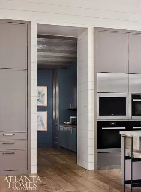Modern kitchen with gray cabinetry, stainless steel appliances, and a view into a dark blue pantry with wood plank ceiling and artwork