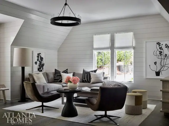 Living room with gray sectional sofa, two brown swivel chairs, black side table, and shiplap walls.