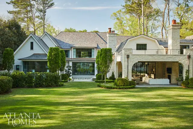 Modern home with white stucco and stone facade, large windows, and manicured lawn. Features an arched covered patio with outdoor seating.