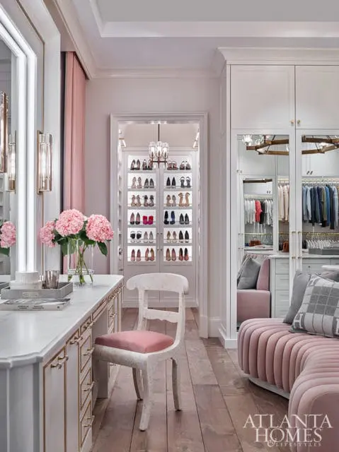 White closet with pink velvet seating, marble vanity, and illuminated shoe displays.