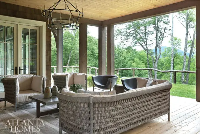 Covered porch with wicker sofas and chairs, a dark metal chandelier, and a view of lush green trees and mountains.