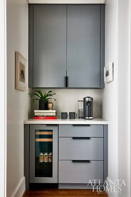 Gray built-in bar with a wine fridge, coffee maker, stacked books, and framed art on the wall.