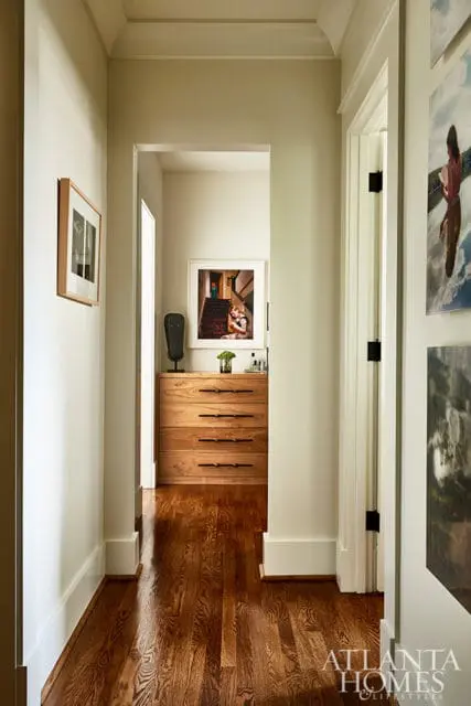 Hallway with light green walls, dark wood floors, and a wooden dresser with black hardware. Artwork hangs on the walls.