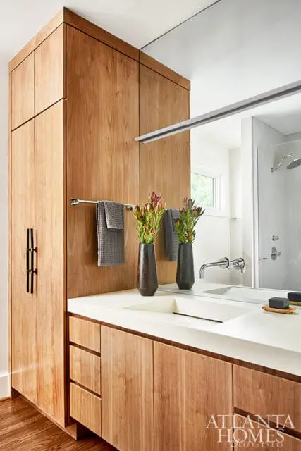 Modern bathroom with light wood vanity cabinets, white countertop with integrated sink, and tall wood storage cabinet with black hardware.