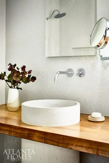Modern bathroom with a concrete vessel sink on a wooden vanity, chrome wall-mounted faucet, and a large mirror reflecting a shower head.